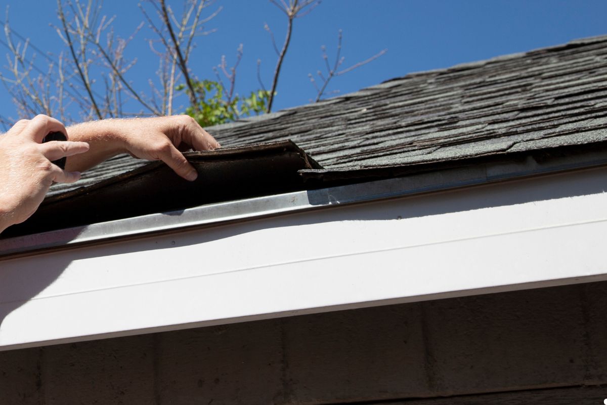 A man repairs a house roof using a tool, focused on his work while standing on a ladder.