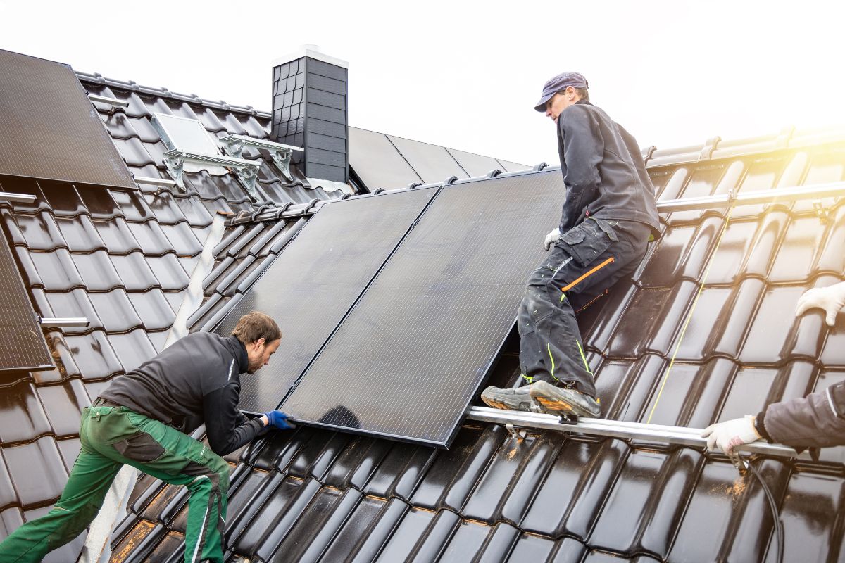 Two workers on a roof in Washington State, installing a solar panel, emphasizing the home's new look and energy efficiency.