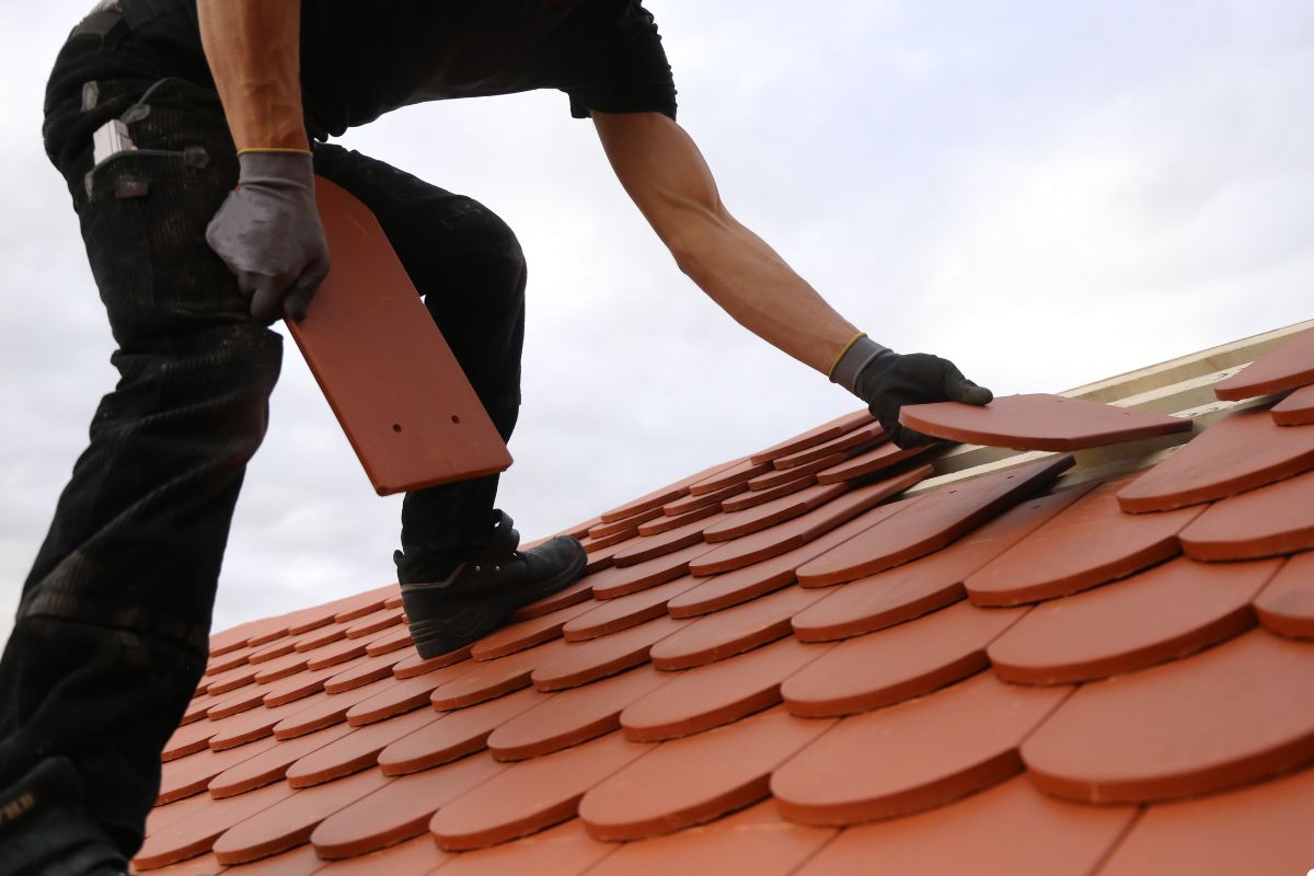 A man is engaged in the process of installing a roof tile, showcasing his expertise in roofing work.